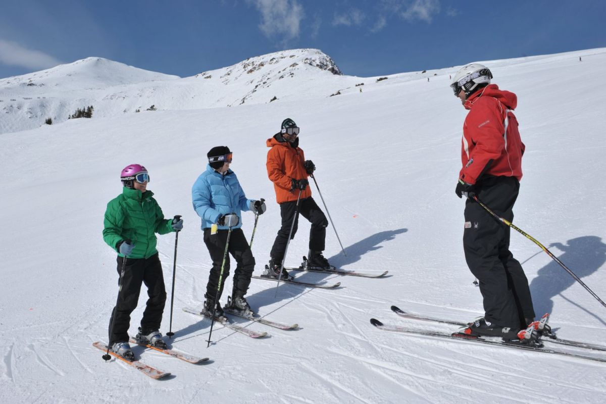 Ski Instructor in red jacket teaches adult group ski lesson